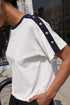 Person wearing a white t-shirt with black trim and buttons outdoors.