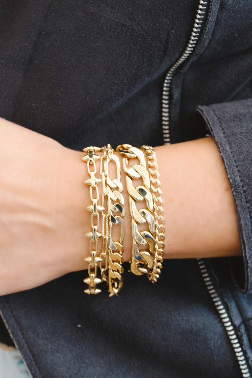 Gold chain bracelets on a wrist with a dark jacket background