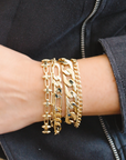 Gold chain bracelets on a wrist with a dark jacket background