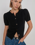 Woman wearing a black short-sleeve button-up shirt and blue jeans against a plain background