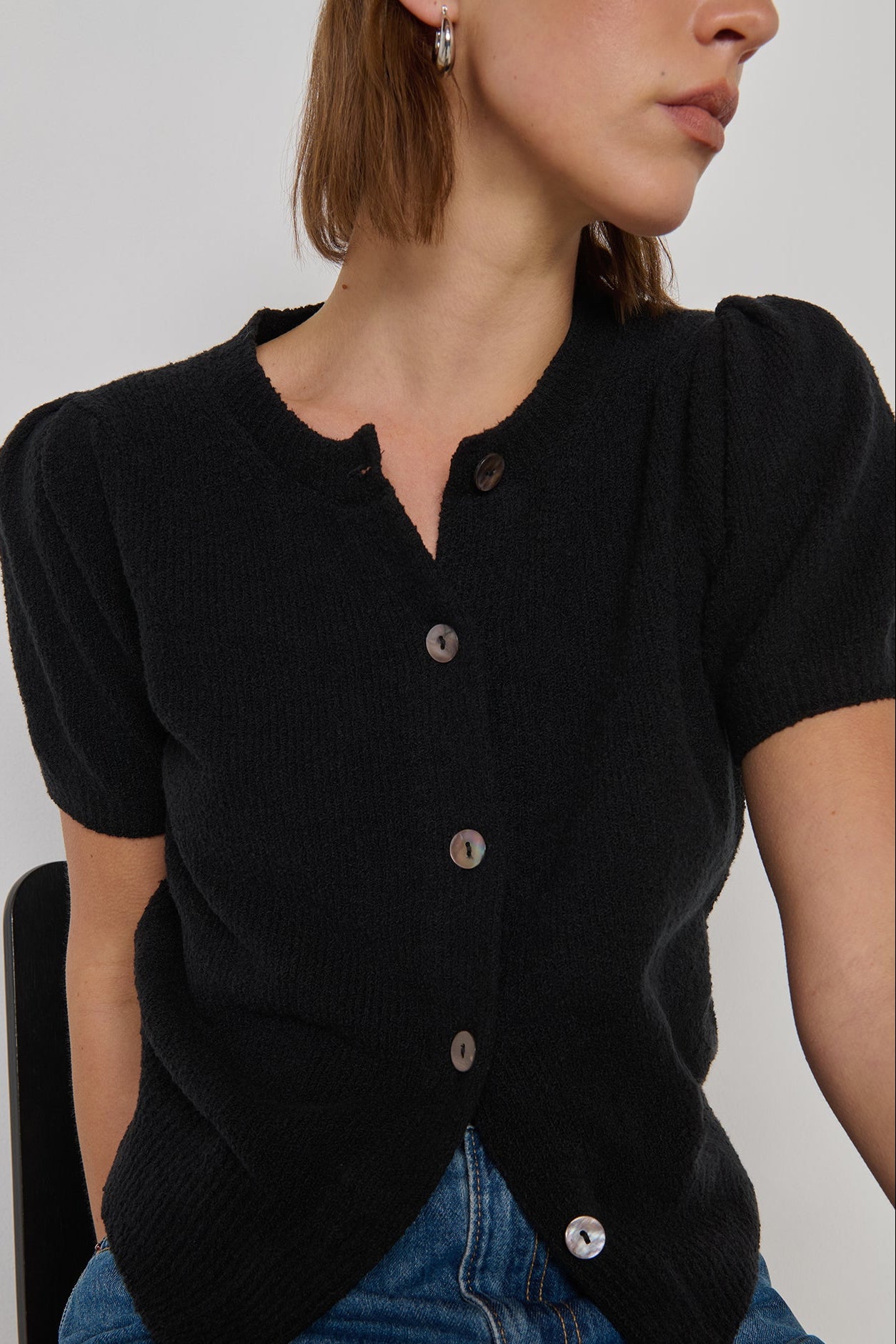 Person wearing a black cardigan with buttons on a plain background