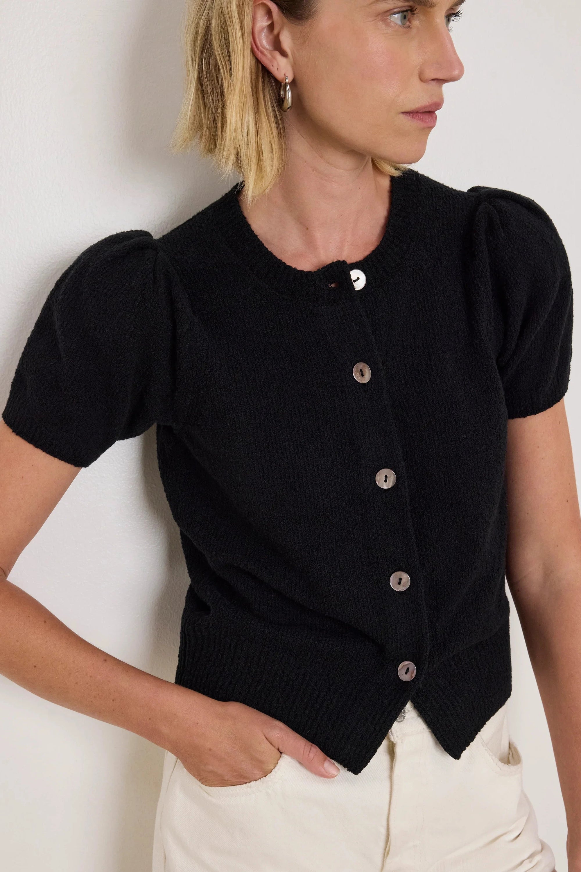 Woman wearing a black short-sleeve cardigan with buttons against a white background