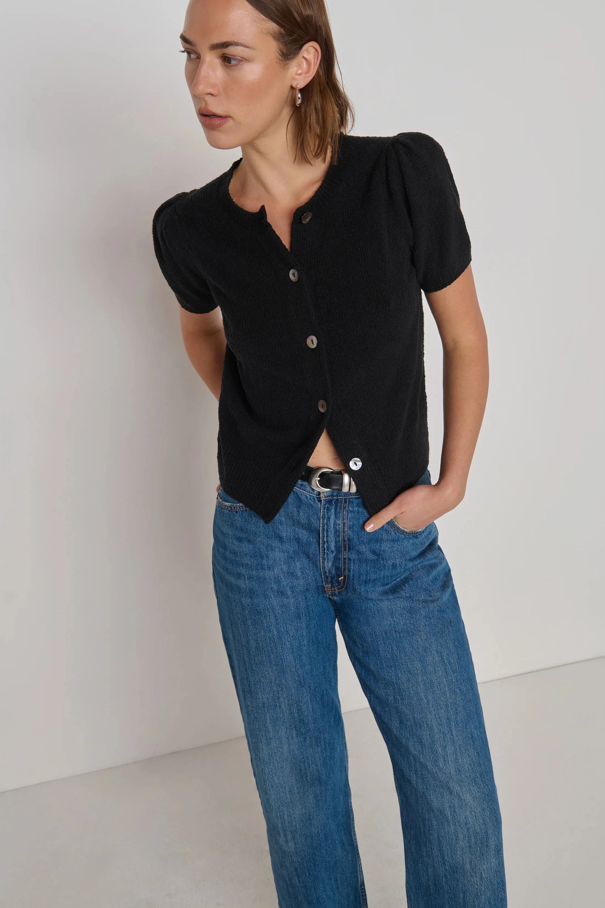 Woman wearing a black top and blue jeans against a white background