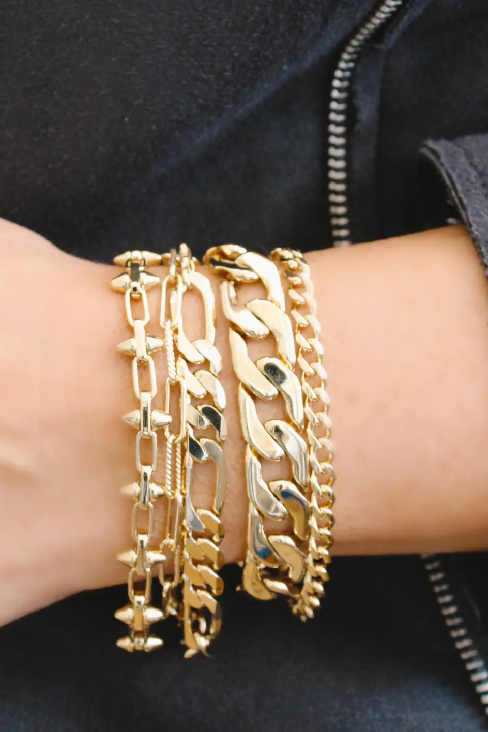 Gold chain bracelets on a wrist with a dark background