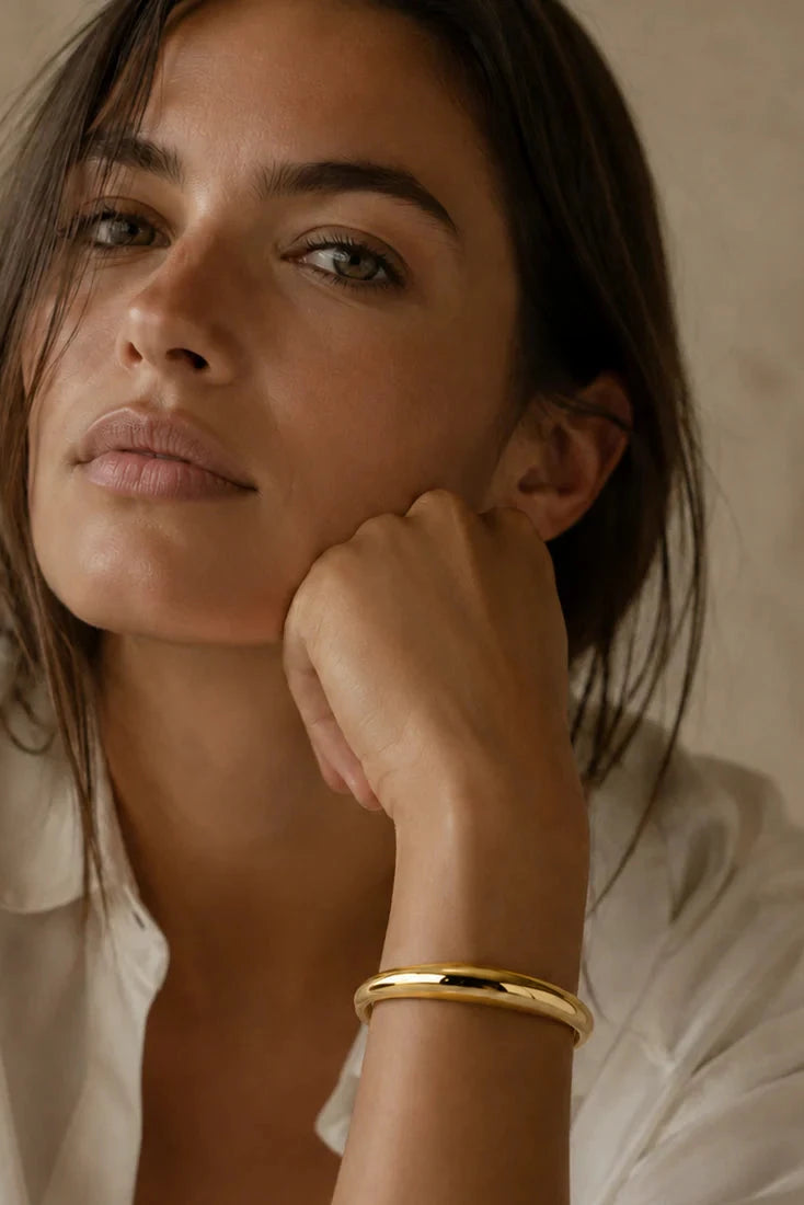Woman wearing a gold bracelet with a neutral background