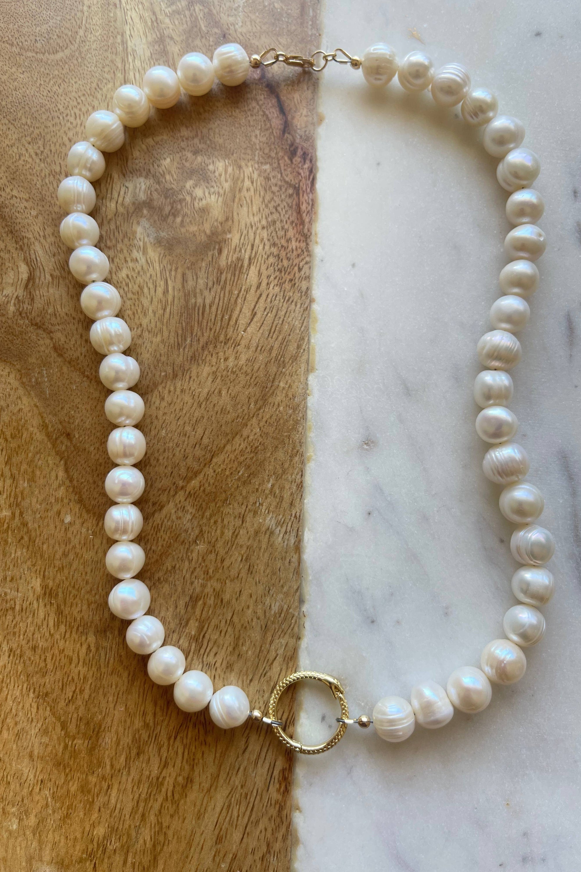 Pearl necklace with gold clasp on a marble and wooden surface