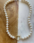 Pearl necklace with gold clasp on a marble and wooden surface
