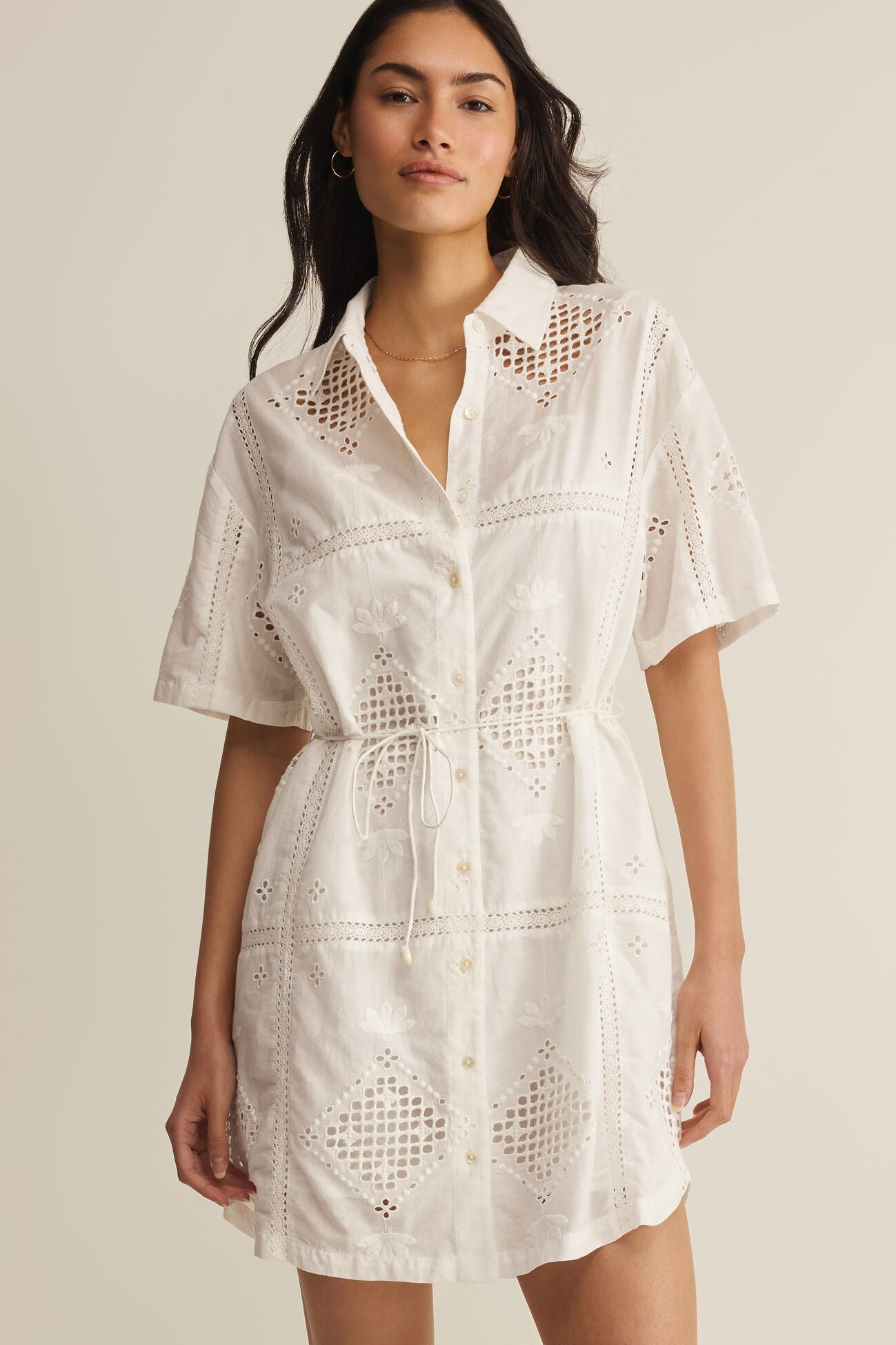 Woman wearing a white lace dress against a beige background
