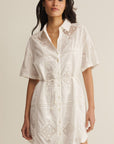Woman wearing a white lace dress against a beige background