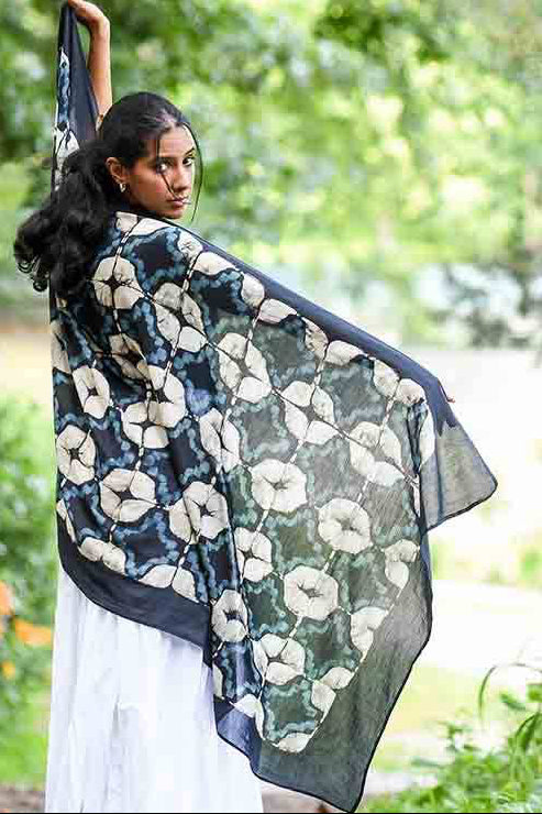 Woman holding a floral-patterned scarf outdoors with greenery in the background