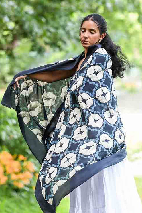 Woman holding a floral-patterned black and white scarf in a garden setting