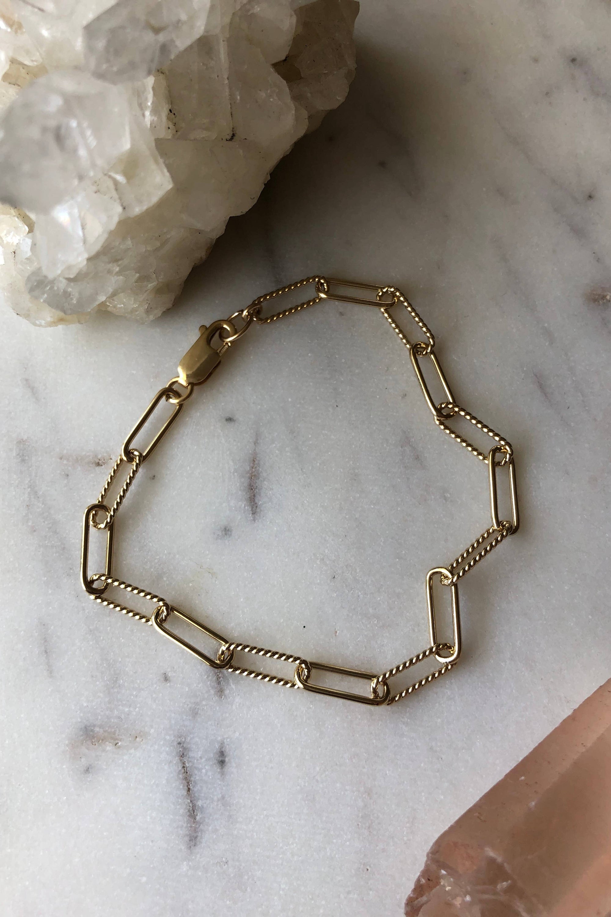 Gold chain bracelet on a marble surface with a hand partially visible