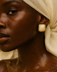 Woman with a beige headscarf and gold earring against a beige background