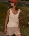 Woman wearing a beige sleeveless top and shorts with a red cap outdoors.