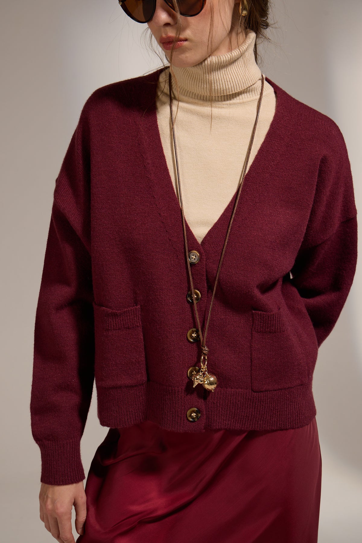 Person wearing a burgundy cardigan over a beige turtleneck with a plain background