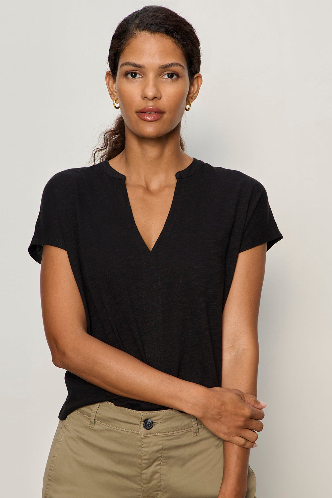 Woman wearing a black t-shirt and beige pants against a plain background