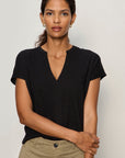 Woman wearing a black t-shirt and beige pants against a plain background