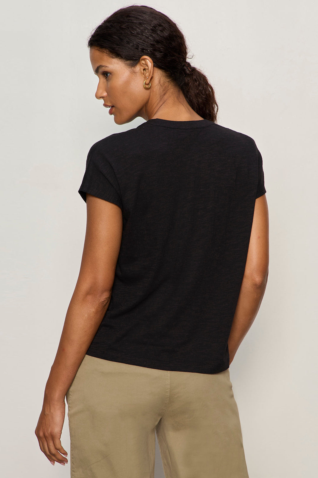 Woman wearing a black t-shirt and beige pants against a plain background