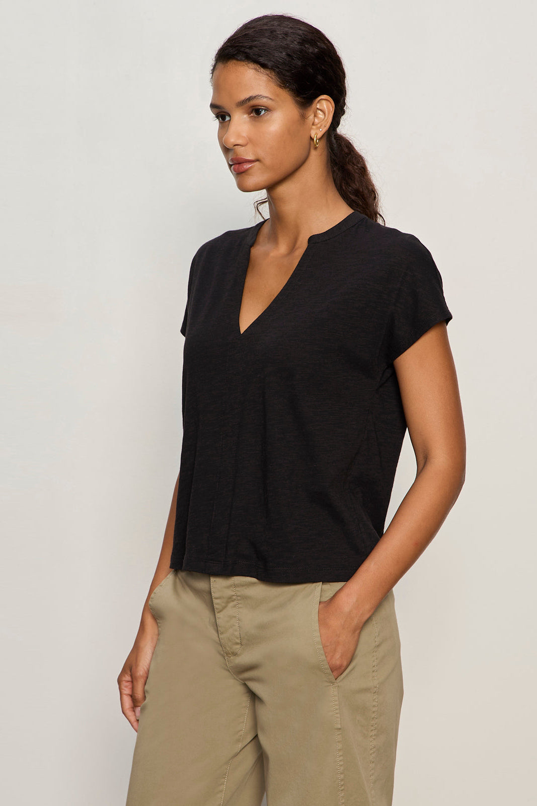 Woman wearing a black V-neck t-shirt and beige pants against a plain background
