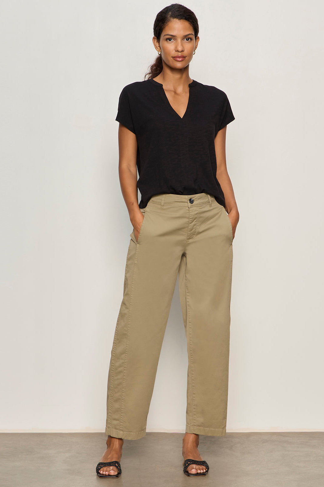 Woman wearing a black top and beige pants against a white background