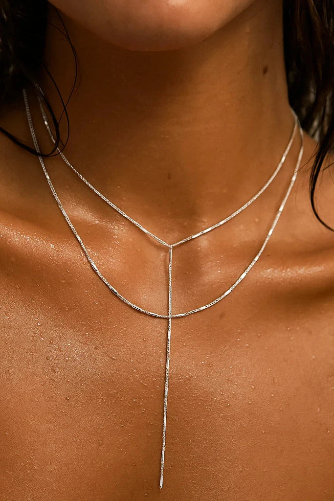 Close-up of a person wearing a thin silver necklace on a neutral background