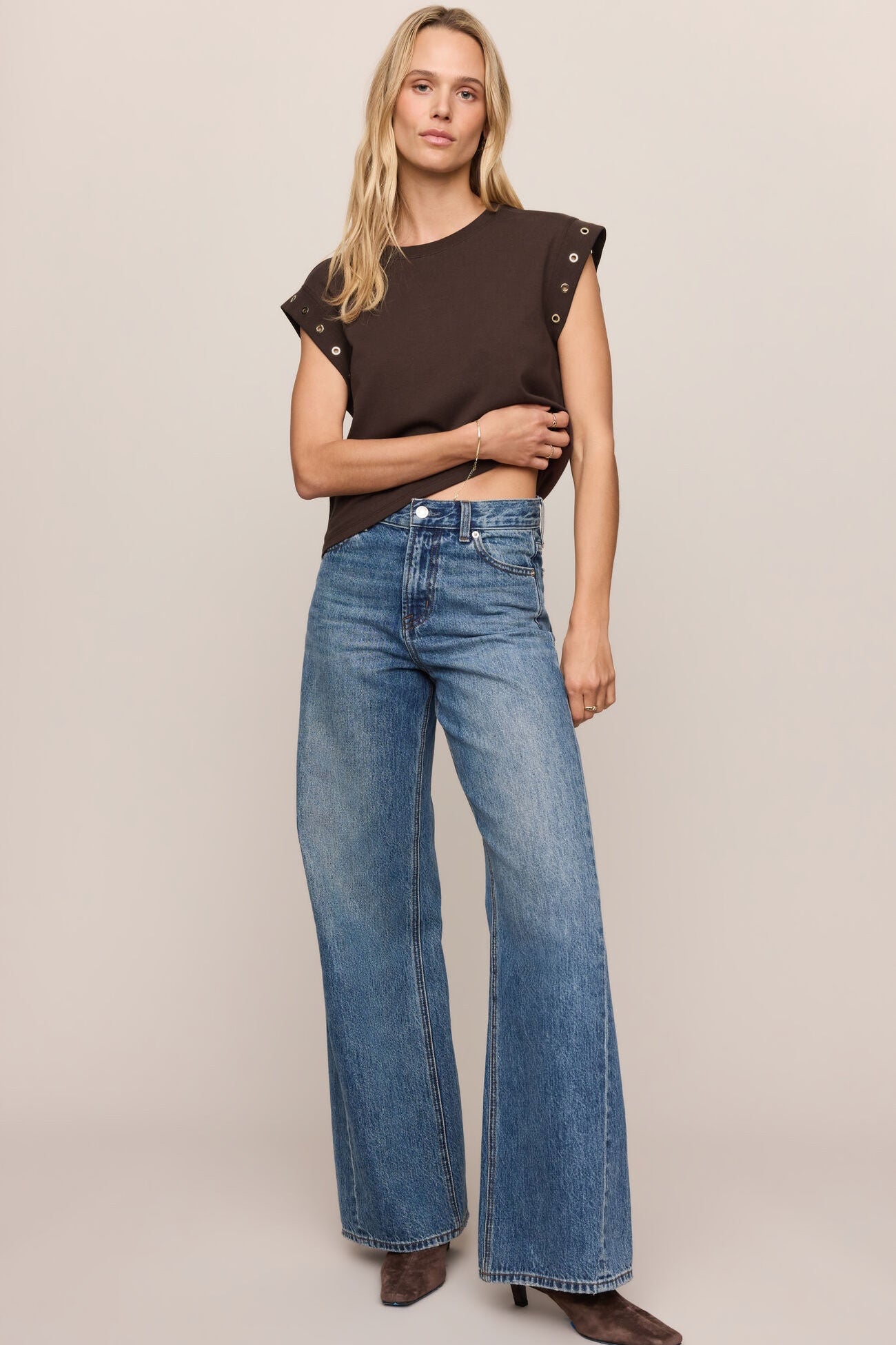 Woman wearing a brown top and blue jeans against a beige background