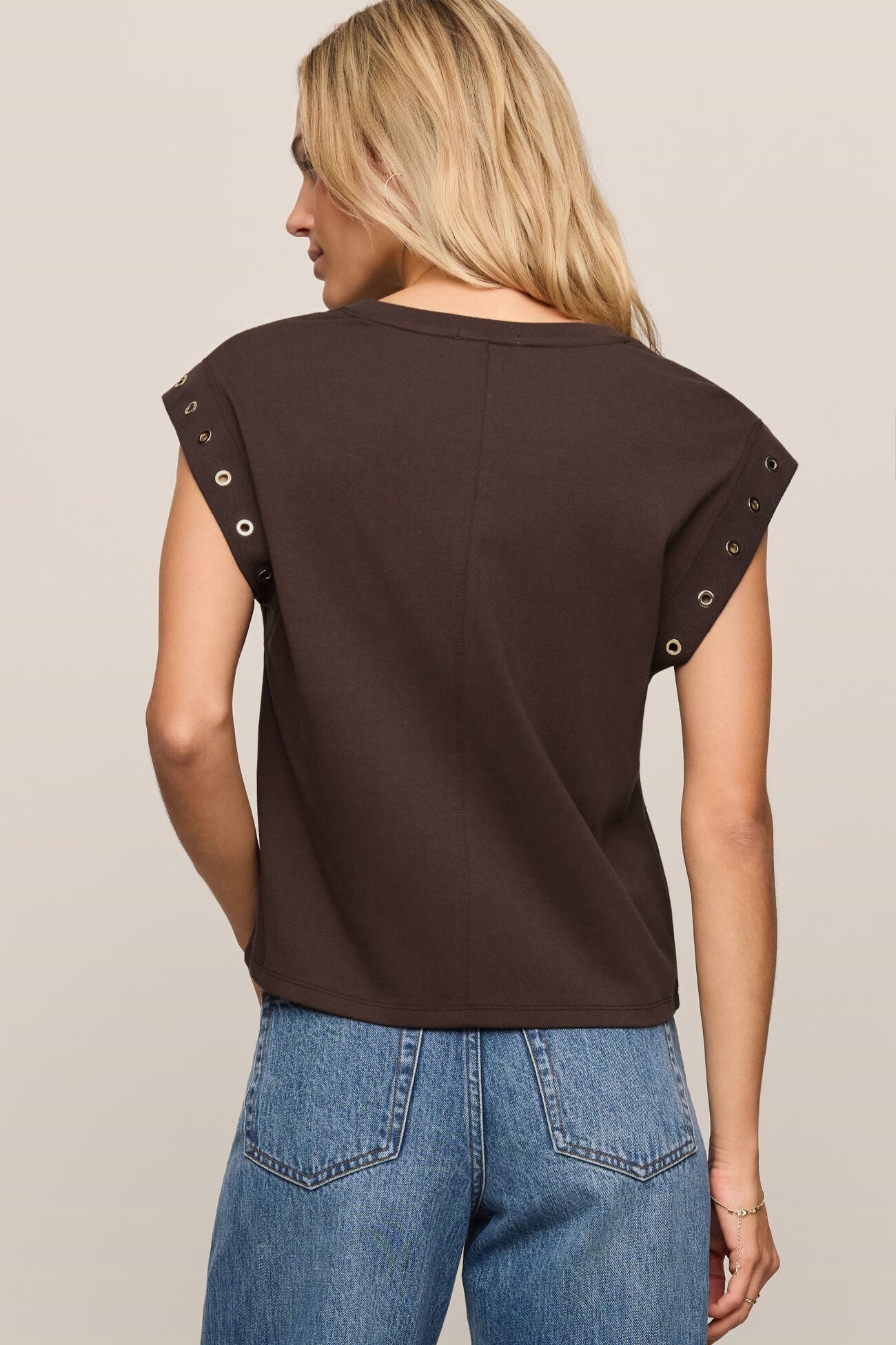 Woman wearing a brown sleeveless top with decorative straps on a beige background
