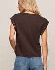 Woman wearing a brown sleeveless top with decorative straps on a beige background
