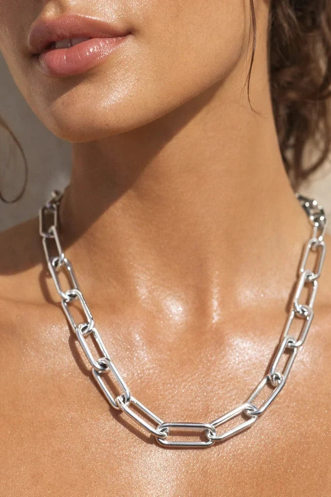 Close-up of a woman wearing a silver chain necklace with a neutral background
