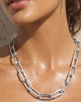 Close-up of a woman wearing a silver chain necklace with a neutral background