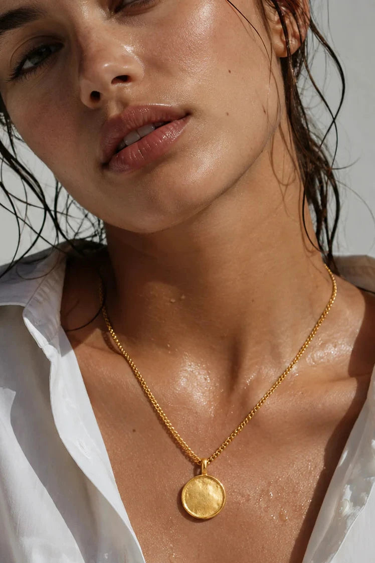 Woman wearing a gold necklace with a coin pendant, close-up of her neck and shoulders.