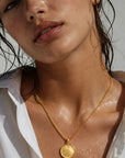 Woman wearing a gold necklace with a coin pendant, close-up of her neck and shoulders.
