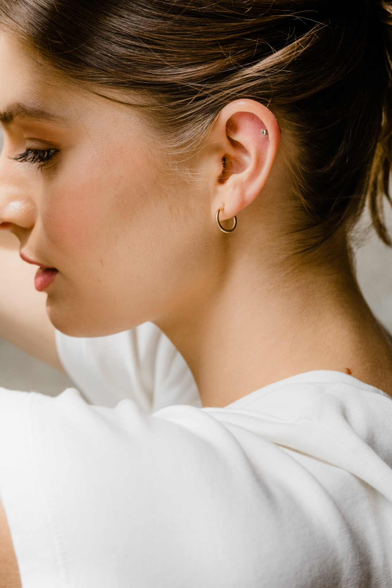 Close-up of a person wearing a small hoop earring with a neutral background