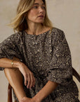 Woman wearing a patterned dress sitting on a chair against a beige background