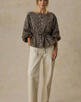 Woman wearing a patterned top and beige pants on a beige background