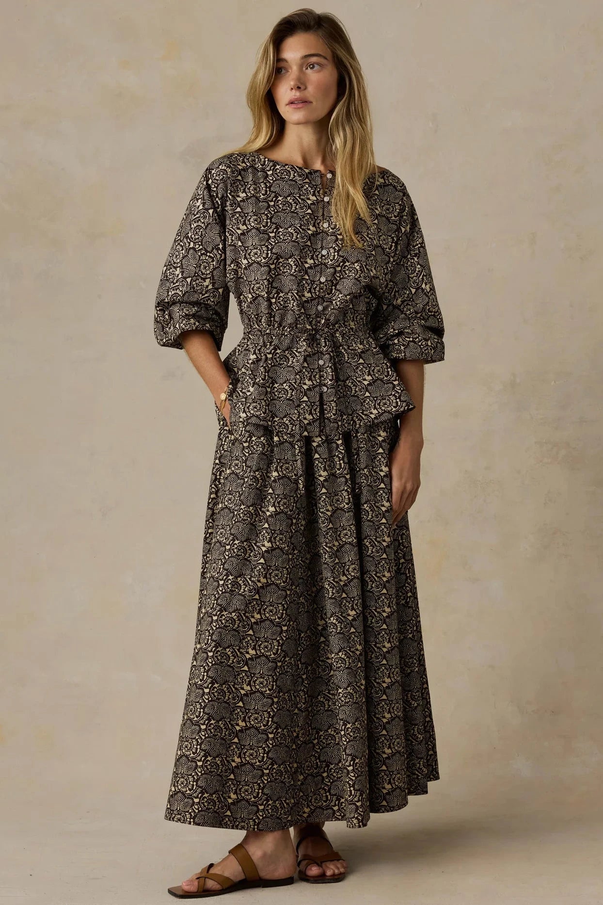 Woman wearing a long, patterned dress against a beige background
