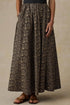 A high-waisted, full-length maxi skirt with an intricate dark brown and beige floral jacquard pattern, shown on a model wearing brown leather sandals against a textured beige studio backdrop.