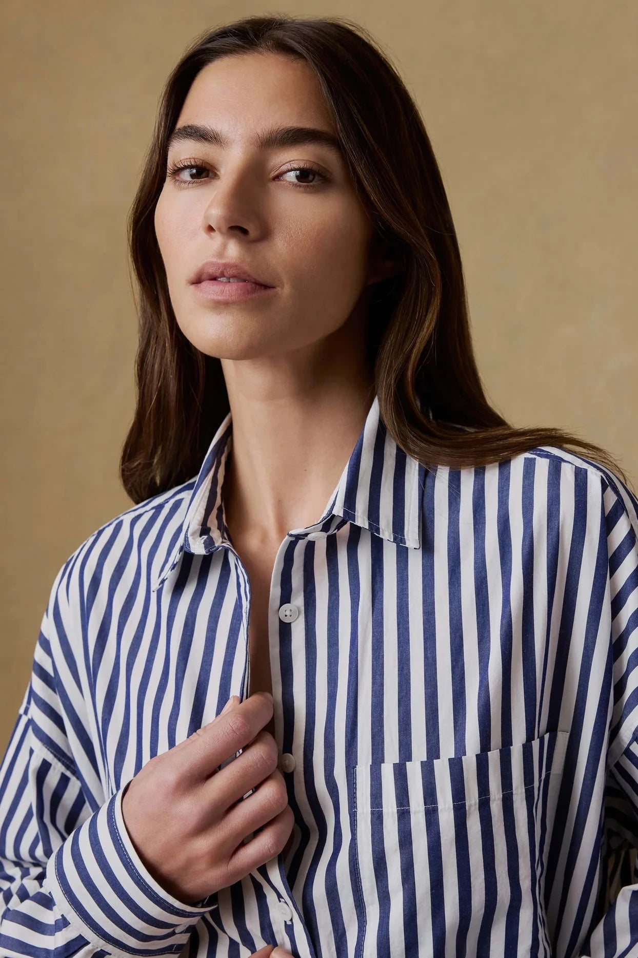 Woman wearing a blue and white striped shirt against a beige background