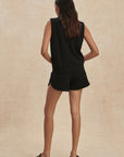 Woman wearing a black sleeveless top and shorts on a beige background