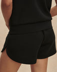 Person wearing a black outfit with shorts on a beige background