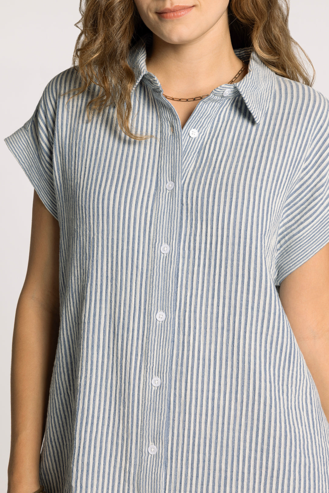 Woman wearing a short-sleeve, button-up shirt with a blue and white striped pattern on a plain background.