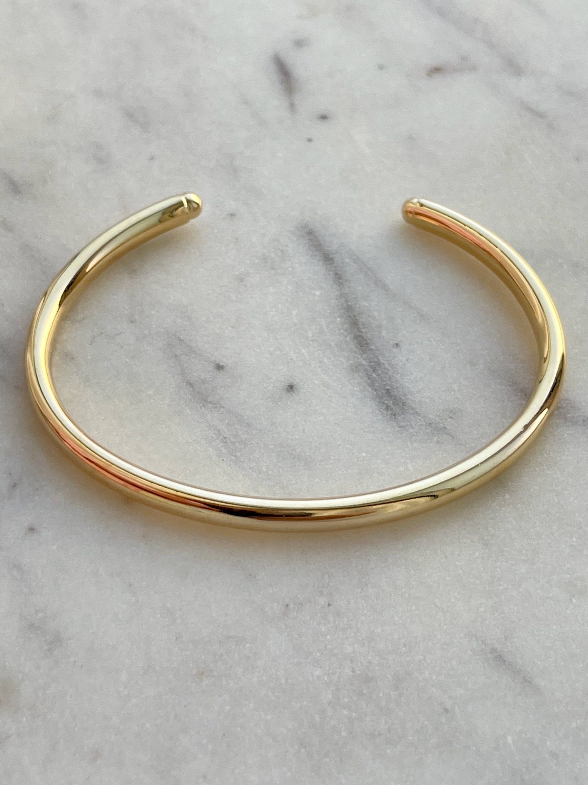 A gold filled smooth round cuff bracelet displayed on a marble surface.