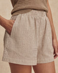 Person wearing a textured brown top and plaid shorts on a beige background