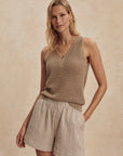 Woman wearing a brown knitted tank top and beige shorts against a beige background