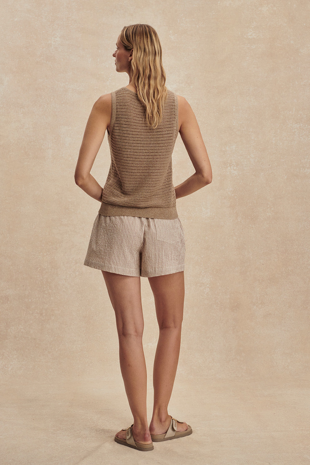 Woman wearing a brown sleeveless top and beige shorts against a beige background