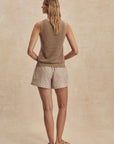 Woman wearing a brown sleeveless top and beige shorts against a beige background