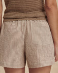 Person wearing a brown textured top and beige shorts against a beige background