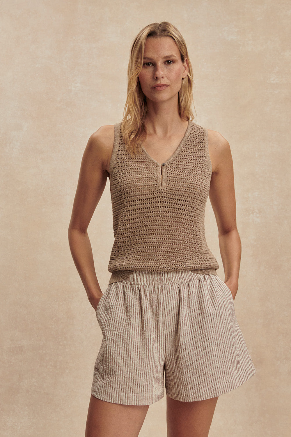Woman wearing a brown knitted tank top and beige shorts against a beige background