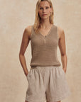 Woman wearing a brown knitted tank top and beige shorts against a beige background