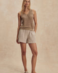Woman wearing a beige sleeveless top and shorts on a beige background